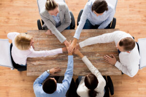 close up of creative team sitting at table and holding hands on top of each other in office after coming to agreement on the importance of Non-dues revenue and revenue diversification