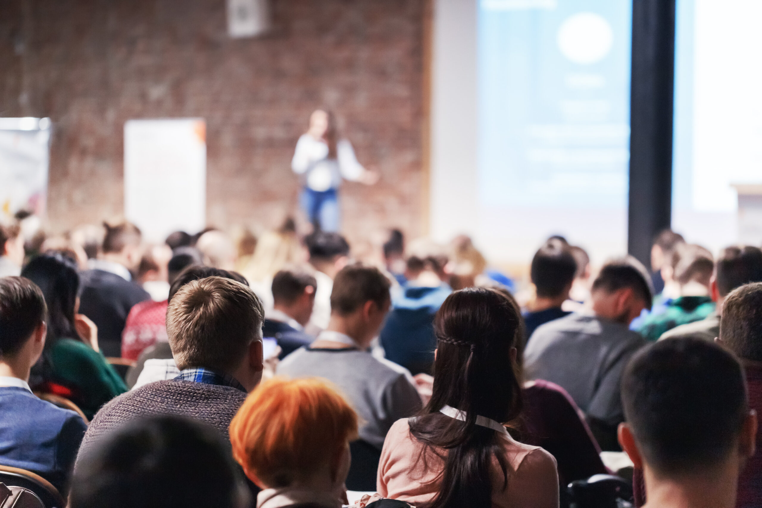 Rows of adult people listening to a woman, meetings professional speak